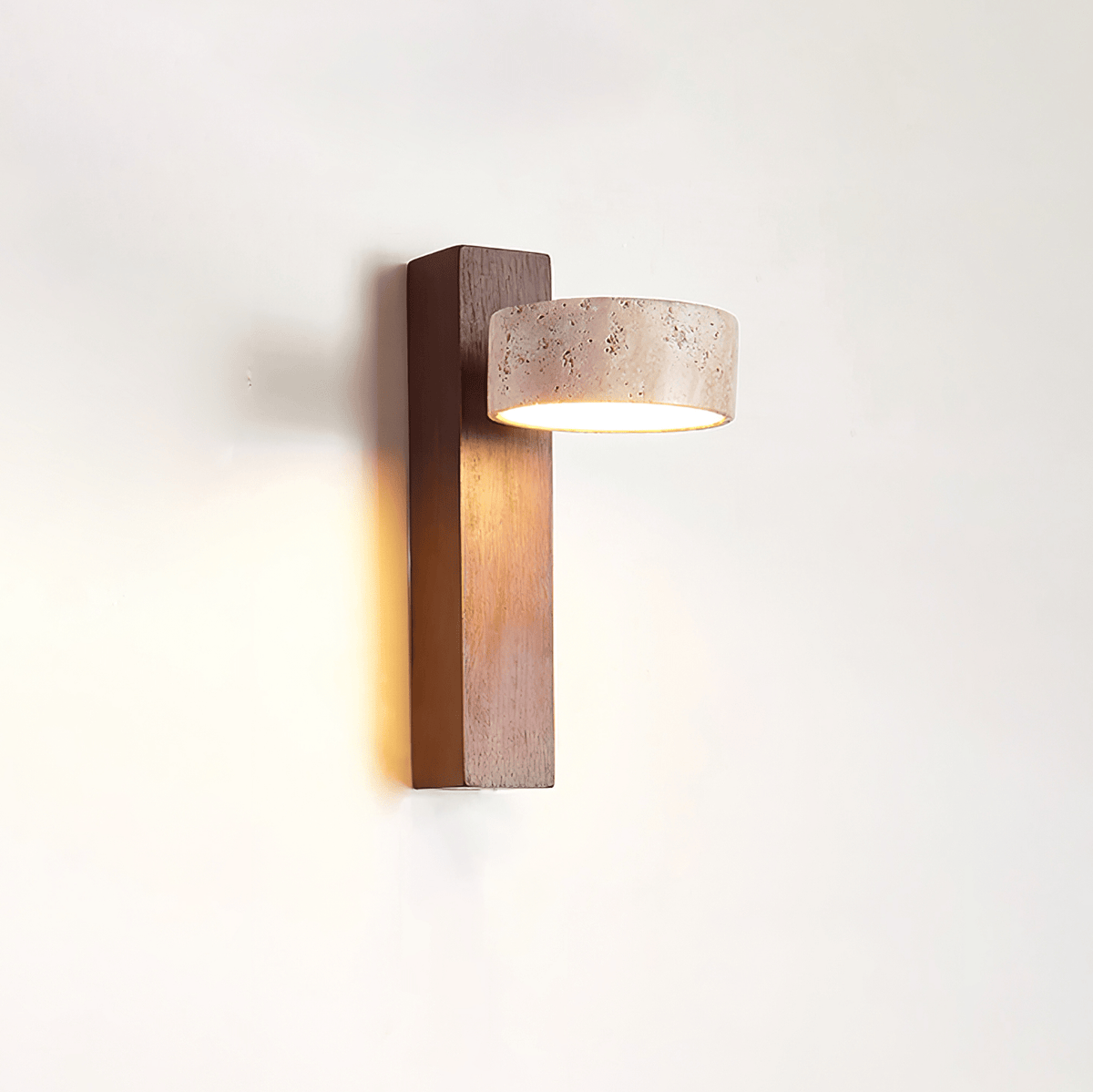 Side view of this Clérachic wall light, with a dark walnut-coloured bar and a travertine head facing out, glowing warm on a white wall.