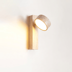 A Clérachic wall light in pale wood with its travertine head angled upwards, lit softly against a plain white wall.