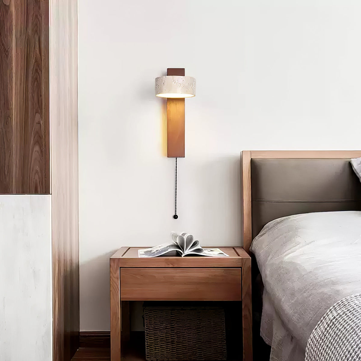 Beside a bed with a grey headboard and a walnut bedside table, this Clérachic wall light hangs with a pull cord down the wall.