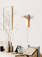 Above a sideboard with vases and a woven basket, this Clérachic wall light in pale wood has a pull cord and sits near a framed twig print.