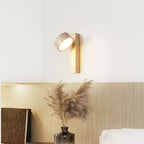 A Clérachic wall light in pale wood with its travertine head tilted up, above a shelf with pampas grass in a dark glass vase.