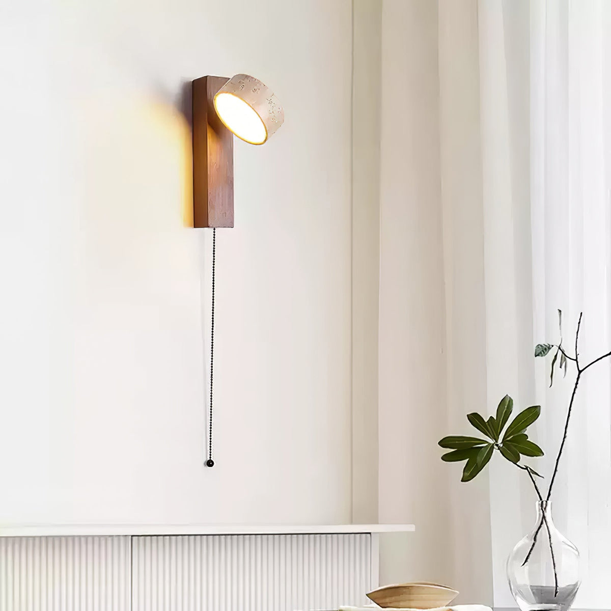 This Clérachic wall light with a walnut-coloured bar hangs by a sheer curtain, its head angled up and a pull cord falling beside a plant.