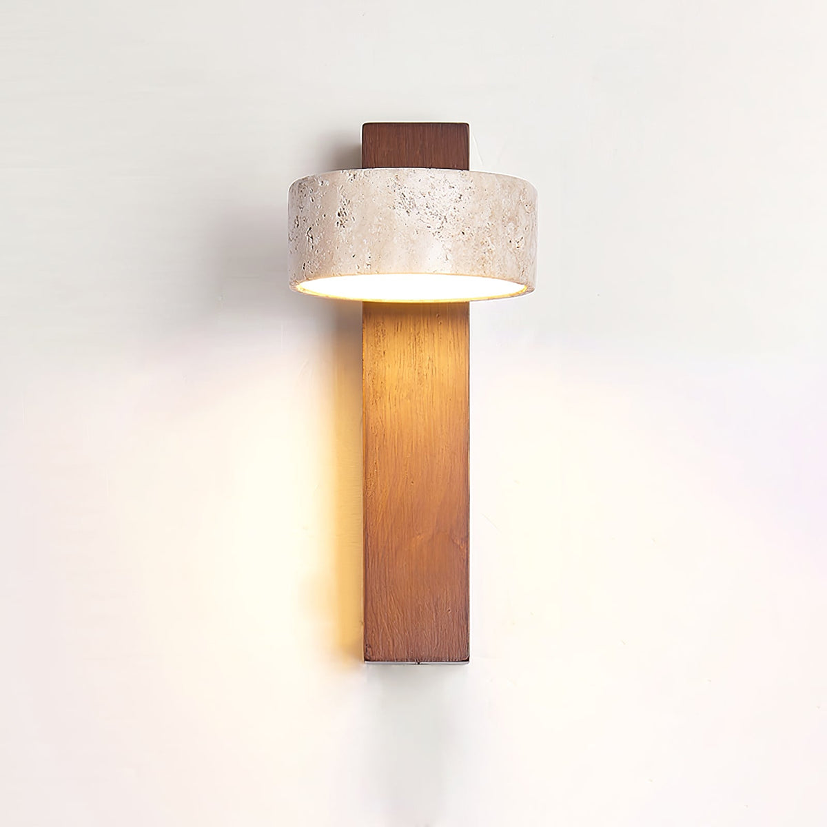 Warm light spreads across the wall behind this Clérachic wall light, which has a walnut-coloured bar and a wide travertine head.