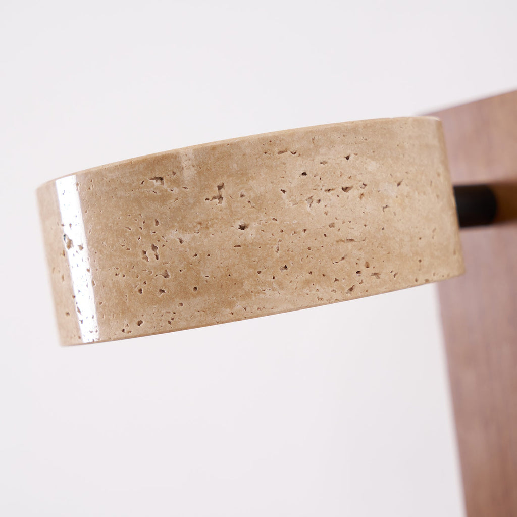 Close view of the pitted travertine surface of the head on this Clérachic wall light, with the wood bar blurred behind it.