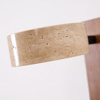 Close view of the pitted travertine surface of the head on this Clérachic wall light, with the wood bar blurred behind it.