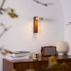 Seen through blurred twigs, this Clérachic wall light with a walnut-coloured bar sits over a sideboard holding books, a cup and a radio.