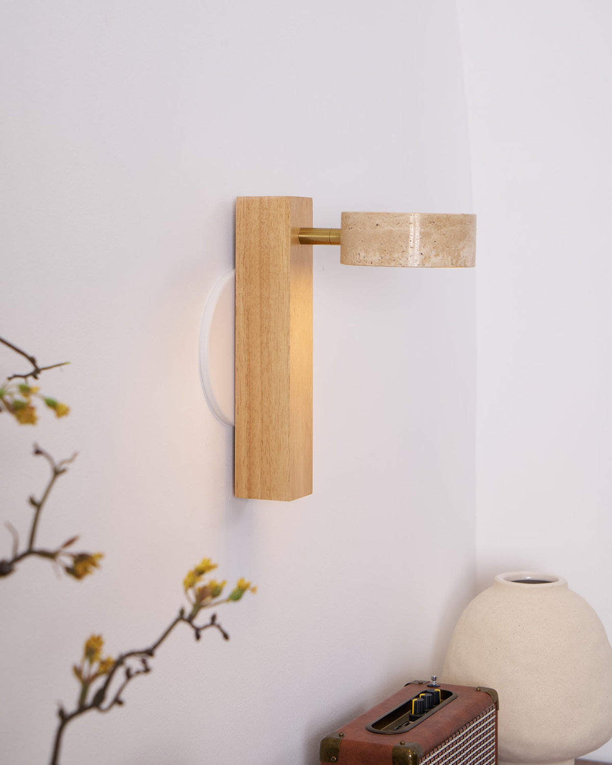 A Clérachic wall light in pale wood with its travertine head swung out sideways, above a retro radio and a cream vase.