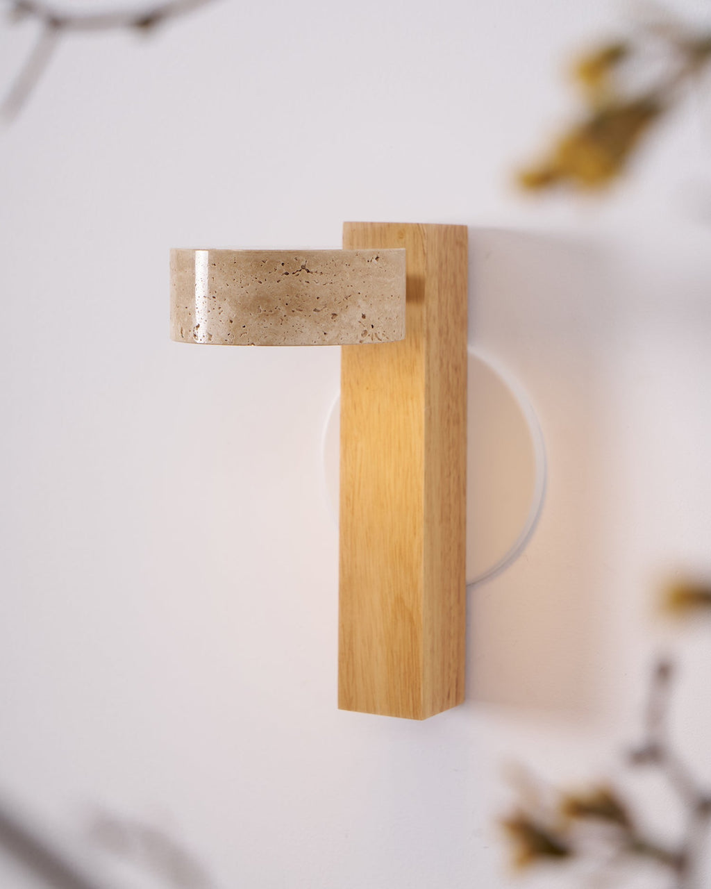 Angled close view of a Clérachic wall light in pale wood, with its travertine head turned out and a round white wall plate behind.
