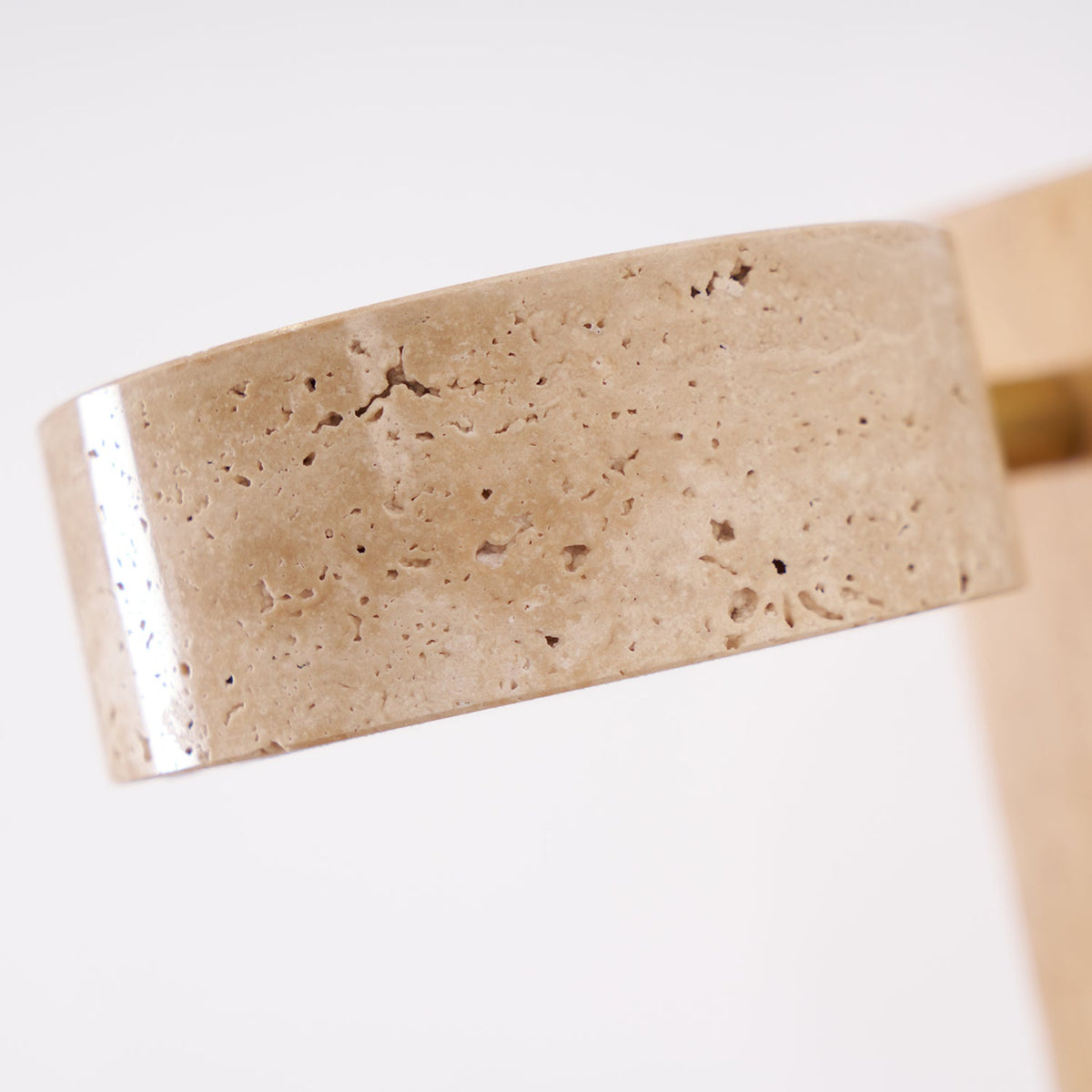 Close view of the pitted, honey-coloured travertine head on this Clérachic wall light, with the pale wood bar at the edge.