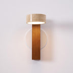 Front view of this Clérachic wall light with a walnut-coloured bar and a travertine head glowing underneath, on a pale wall.