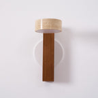 Switched off, this Clérachic wall light has a walnut-coloured bar and a travertine head with a white underside, on a round white plate.