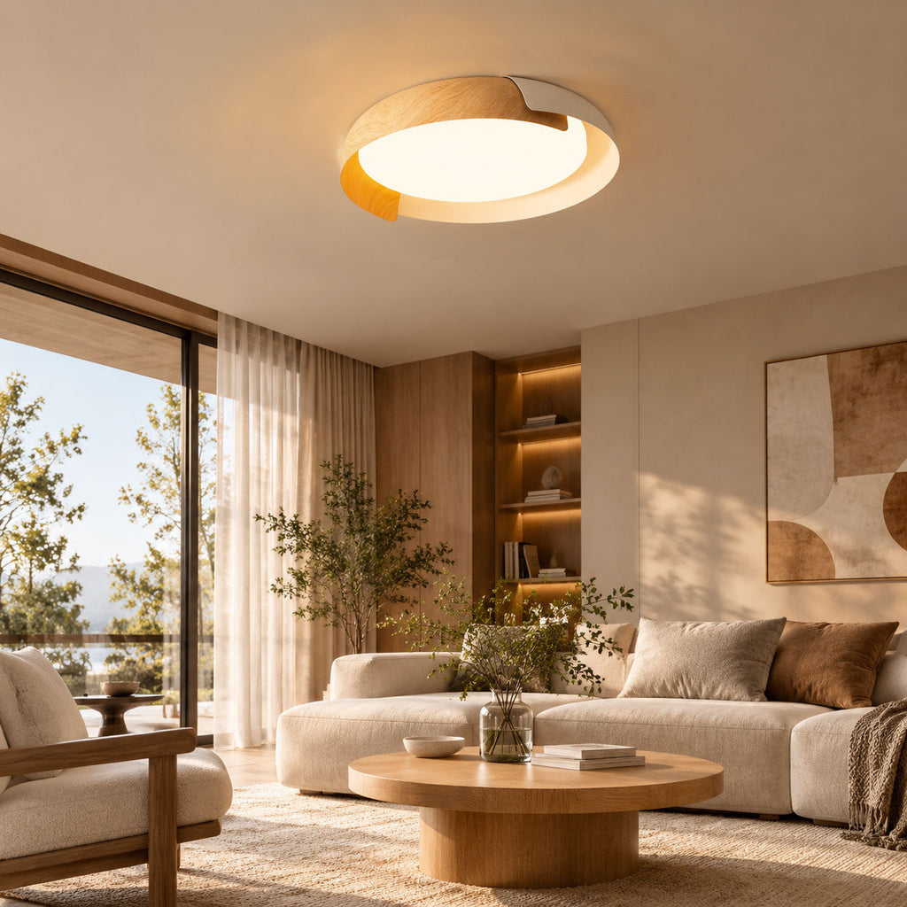 A light wood and white Clérachic ceiling light glows over a cream sofa and round oak coffee table, beside a tall window.
