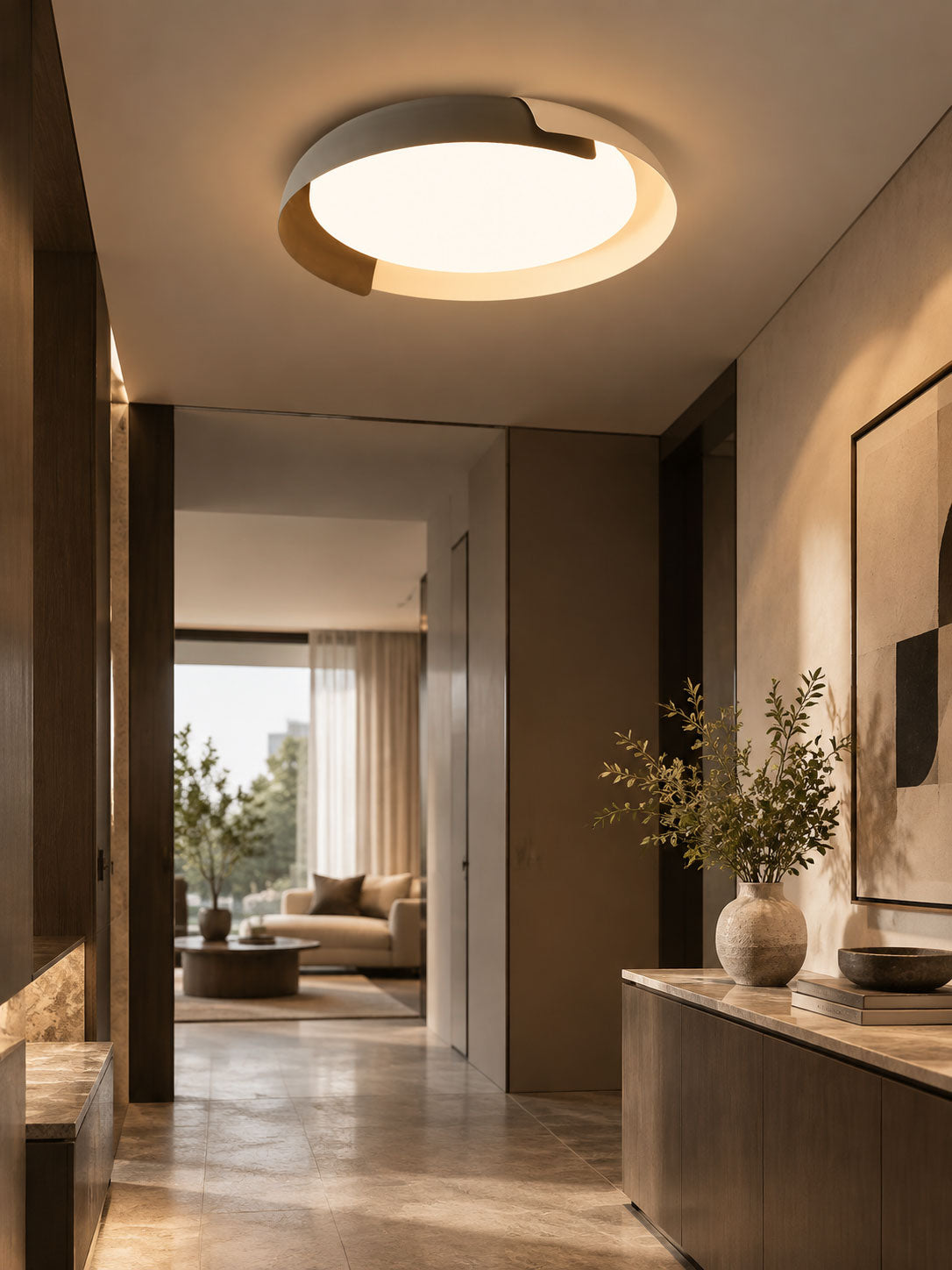 A white and wood Clérachic ceiling light glows over a hallway leading to a bright living room, with a console and olive branches.