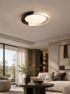 A black and white Clérachic ceiling light glows over a living room with a cream sofa, a dark coffee table and tall windows.