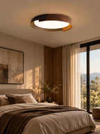 A black and dark wood Clérachic ceiling light glows above a bed with brown linen and sheer curtains, beside a large window.