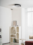 A black and white Clérachic ceiling light above a white arched shelf and a sheer curtain, in a bright minimalist room.