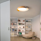 A light wood and white Clérachic ceiling light lit above a white bookcase and a beanbag chair, in a room with a concrete floor.