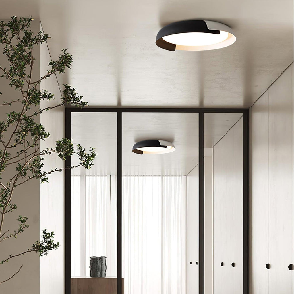 A black and dark wood Clérachic ceiling light lit above a hallway with a glass door, an olive branch and a second light beyond.