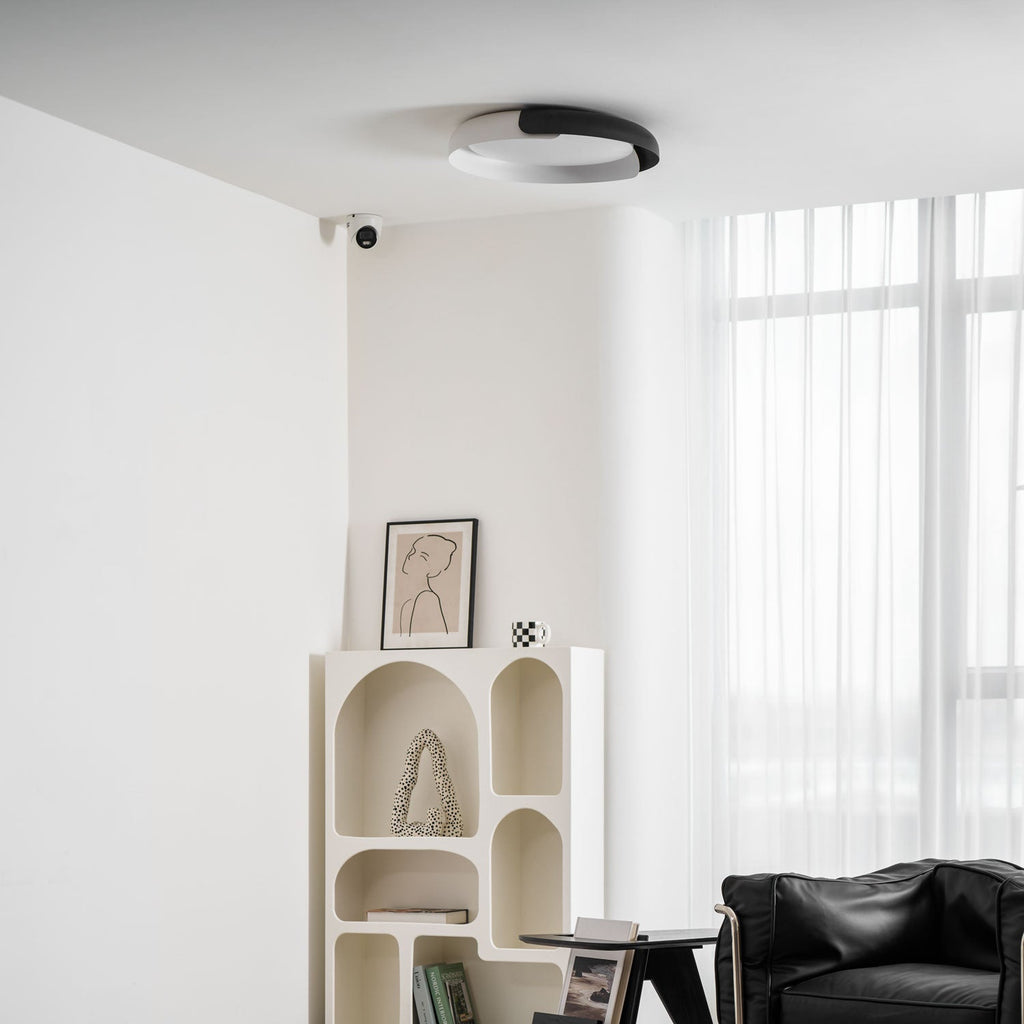 A black and white Clérachic ceiling light above an arched cream shelf, a small side table and a black leather chair.