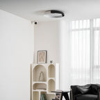 A black and white Clérachic ceiling light above an arched cream shelf, a small side table and a black leather chair.