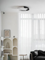 A black and white Clérachic ceiling light above a white arched shelf and sheer curtains, with a leather chair in the corner.