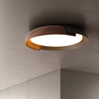 Close view of a dark wood and black Clérachic ceiling light with a frosted lit centre, against a grey ceiling.