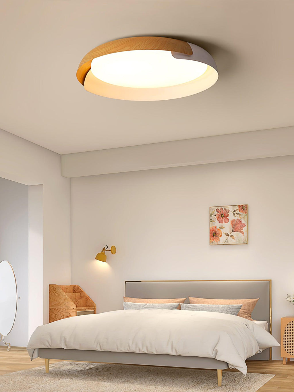 A light wood and white Clérachic ceiling light glows above a bed with peach cushions, in a pale bedroom with a brass wall light.