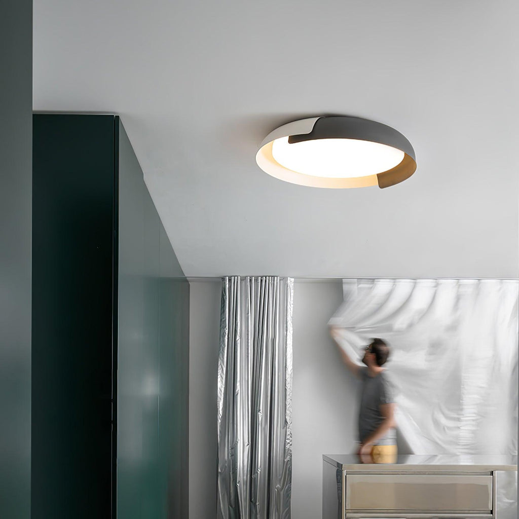 A white and black Clérachic ceiling light lit above a grey room with a dark green wall, where a person is hanging a sheer curtain.