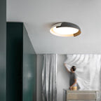 A white and black Clérachic ceiling light lit above a grey room with a dark green wall, where a person is hanging a sheer curtain.