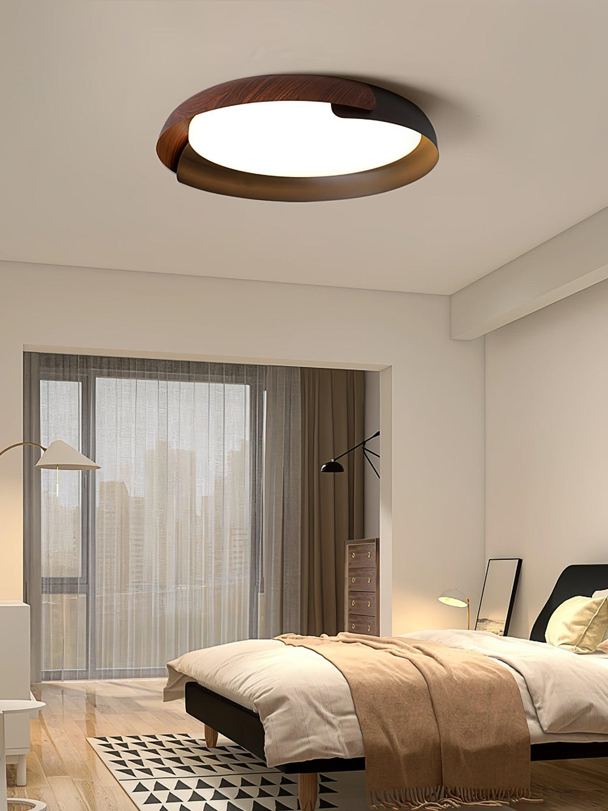 A dark wood and black Clérachic ceiling light lit over a bedroom with a tan throw, a floor lamp and a tall city-view window.