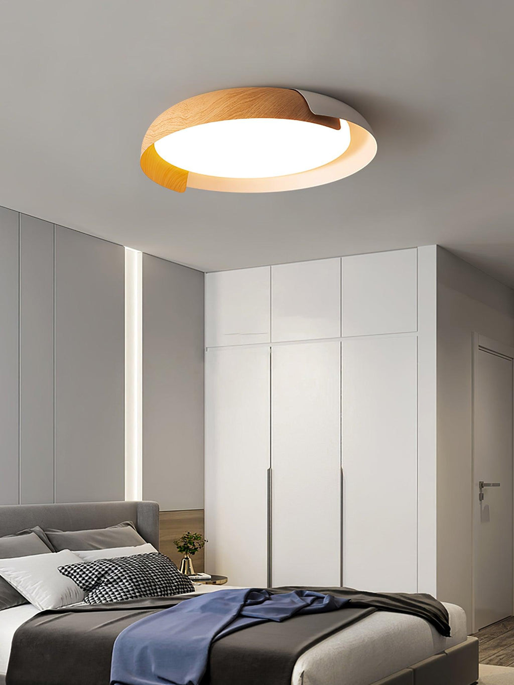 A light wood and white Clérachic ceiling light lit above a grey bed with a navy throw, with a white wardrobe behind.