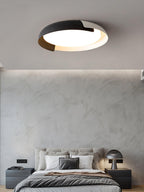 A grey and wood Clérachic ceiling light lit above a bed with dark bedding, a mushroom table lamp and a plaster-effect wall.