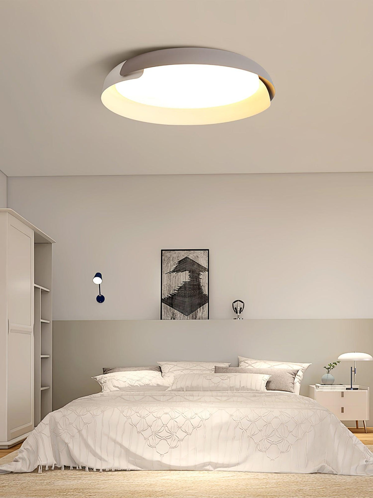 A white and light grey Clérachic ceiling light glows above a bed with white linen and a framed print, in a calm bedroom.