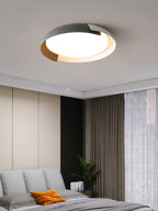 A grey and wood Clérachic ceiling light lit above a bed with grey cushions and an orange pillow, beside brown curtains.