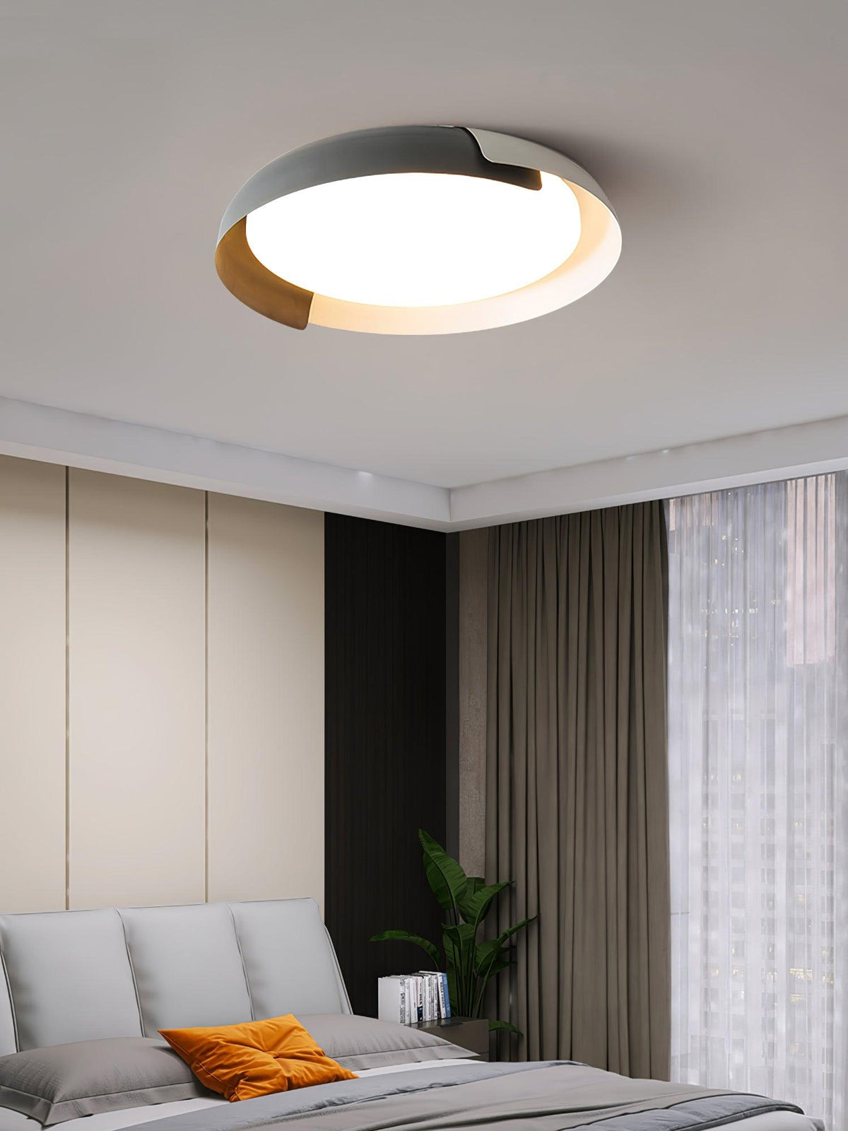 A grey and wood Clérachic ceiling light lit above a bed with grey cushions and an orange pillow, beside brown curtains.