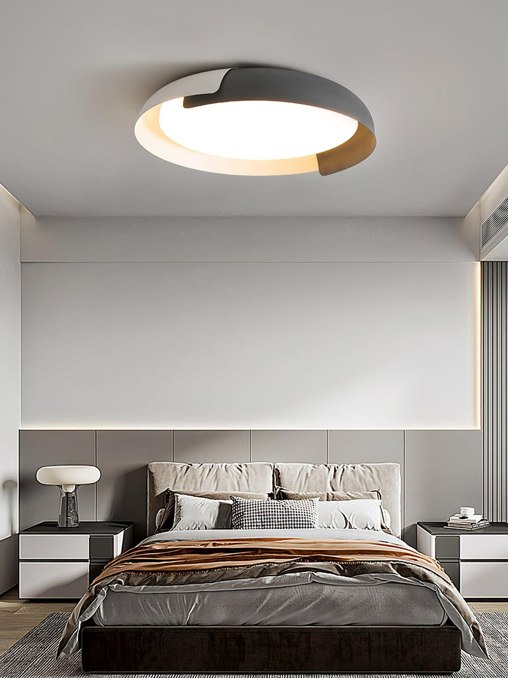 A grey and wood Clérachic ceiling light glows above a bed with a copper-toned throw, in a grey bedroom with a table lamp.