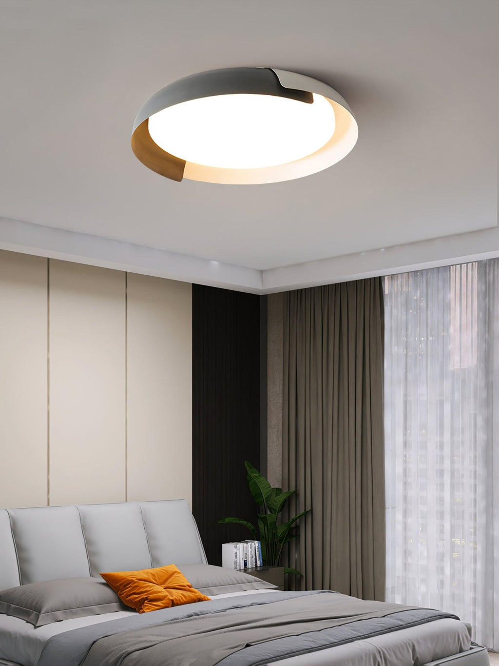 A grey and wood Clérachic ceiling light lit above a bed with an orange pillow, with brown curtains and a green plant.