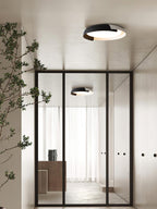 A black and white Clérachic ceiling light lit in a hallway with a glass door, with a second light visible beyond the glass.