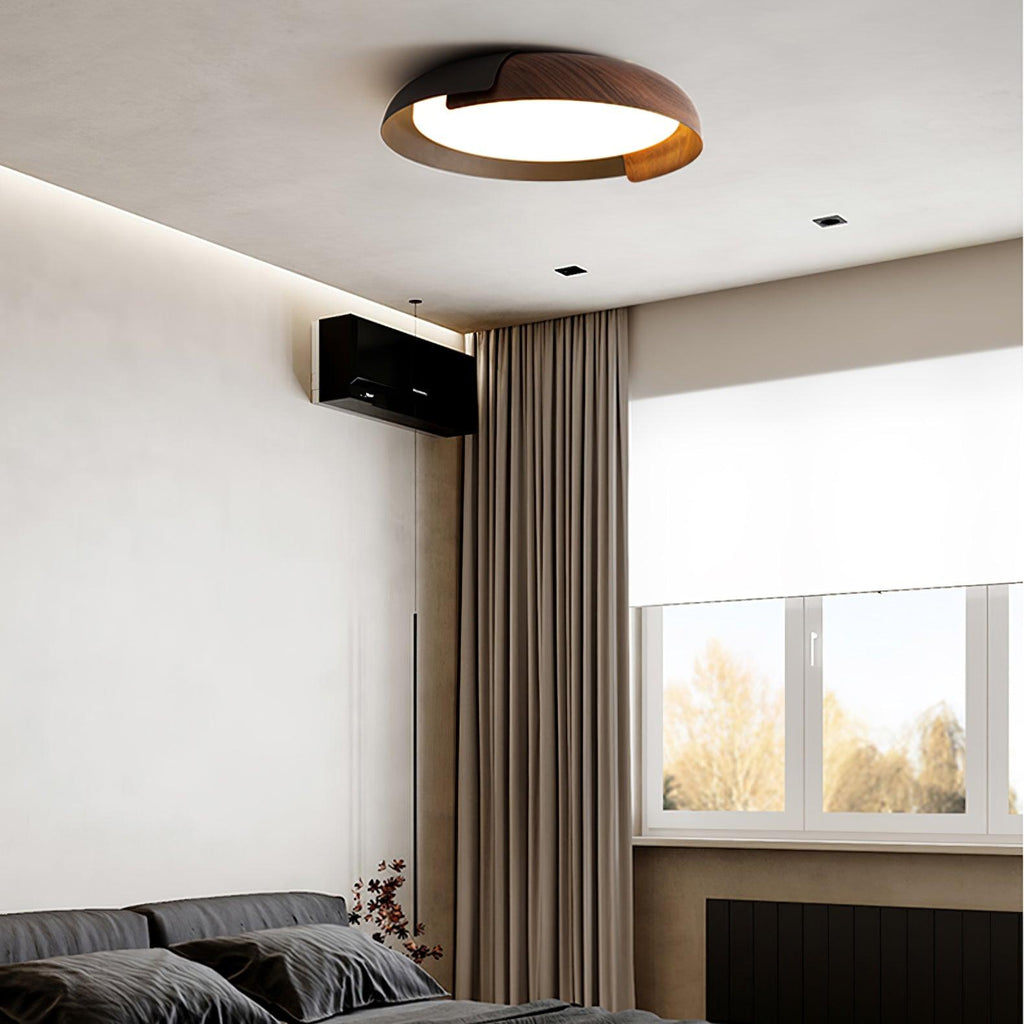A black and dark wood Clérachic ceiling light lit in a bedroom with dark bedding, brown curtains and a window.