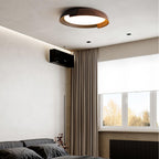 A black and dark wood Clérachic ceiling light lit in a bedroom with dark bedding, brown curtains and a window.