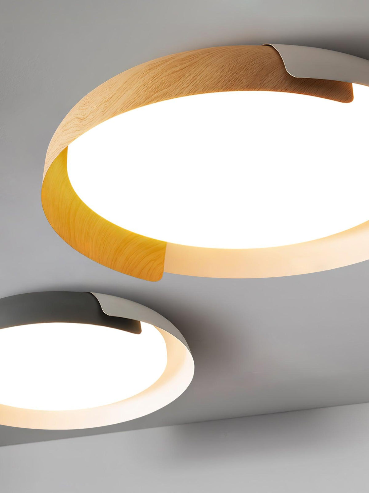 Close view of a light wood and white Clérachic ceiling light with a second grey and wood one below, on a grey backdrop.