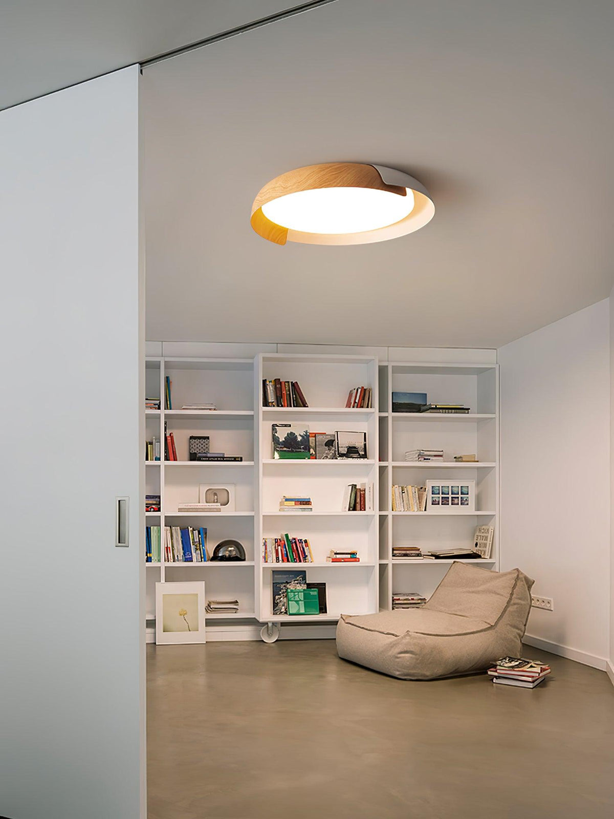 A light wood and white Clérachic ceiling light lit above a bookcase and beanbag chair, seen through a doorway.