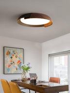 A black and dark wood Clérachic ceiling light lit above a desk with a laptop, orange chairs and a colourful geometric print.