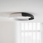 A white and black Clérachic ceiling light, flush to a white ceiling, with a sheer curtain softly visible below.