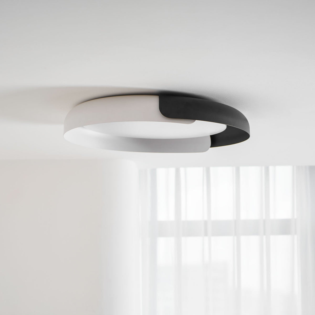 A white and black Clérachic ceiling light, flush to a white ceiling, with a sheer curtain softly visible below.