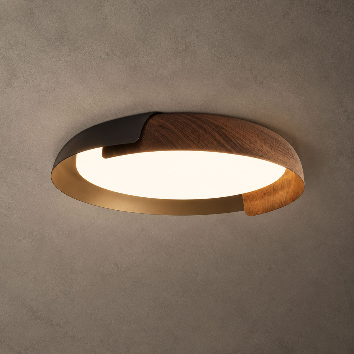 A black and dark wood Clérachic ceiling light with a gold-toned inner rim, lit, against a textured grey-brown ceiling.