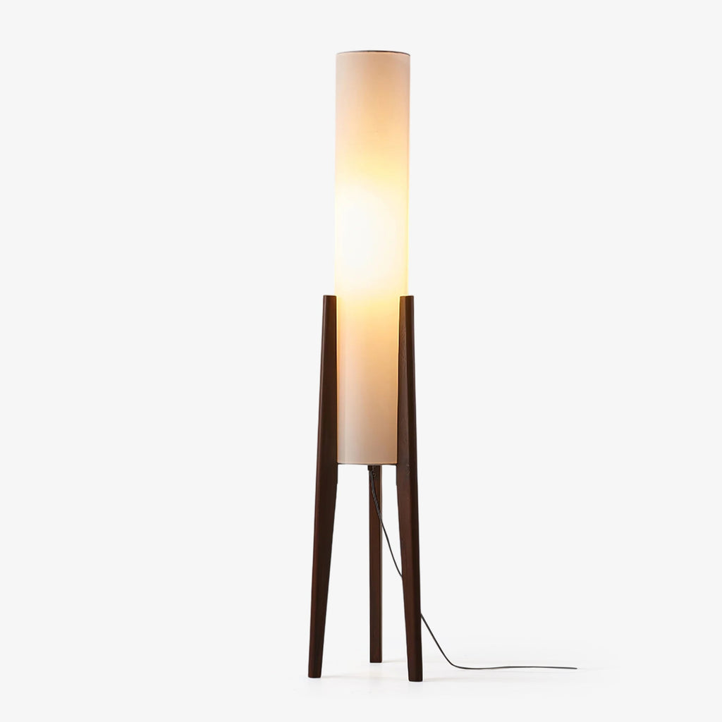 Slim Clérachic floor lamp with a tall white fabric cylinder shade on three dark walnut legs, lit and trailing a black cord on white.