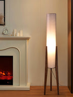 Clérachic floor lamp with a pale shade and walnut legs beside a fireplace with white candles on the mantel.