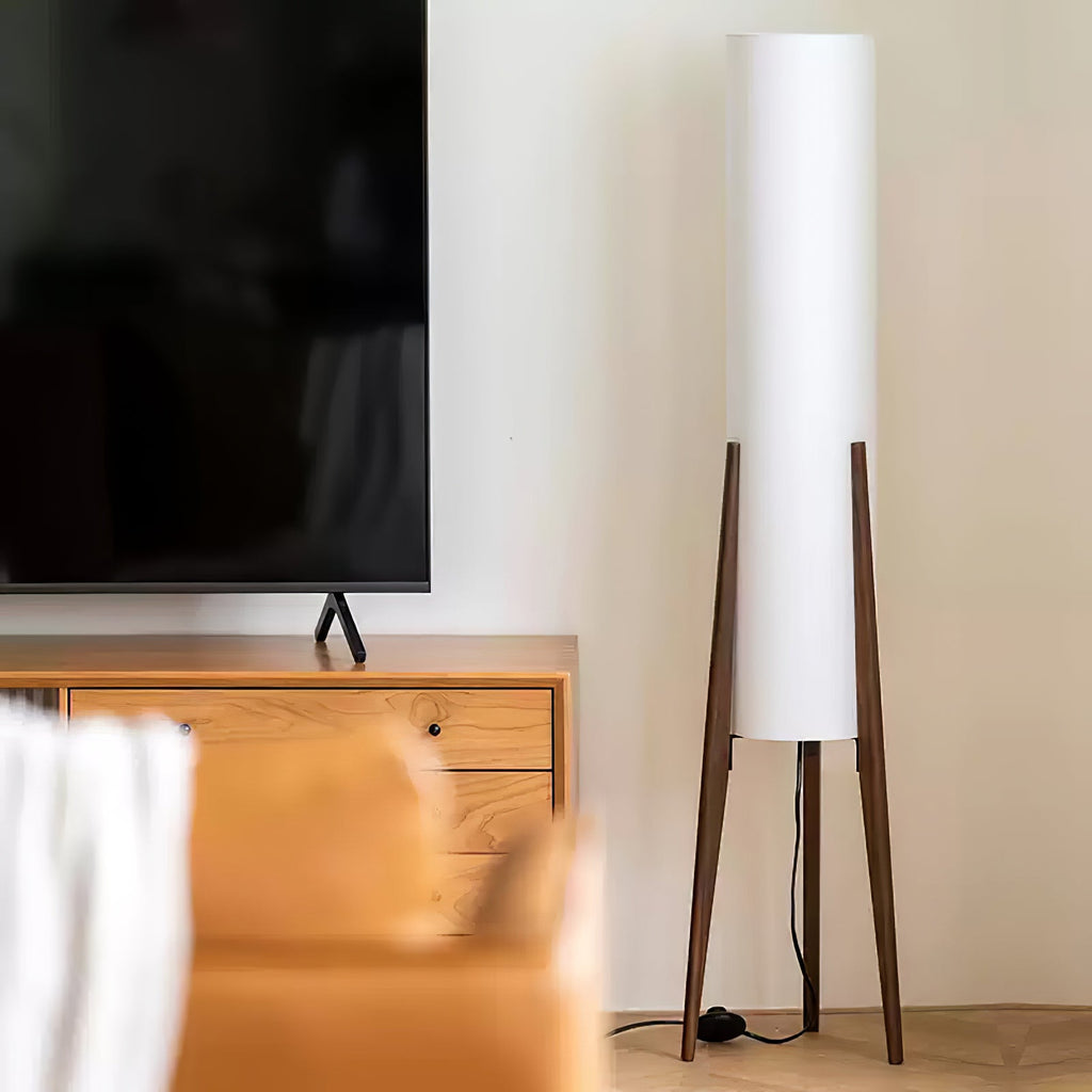 Unlit white cylinder shade on a Clérachic floor lamp with dark walnut legs, beside a TV and an oak cabinet.