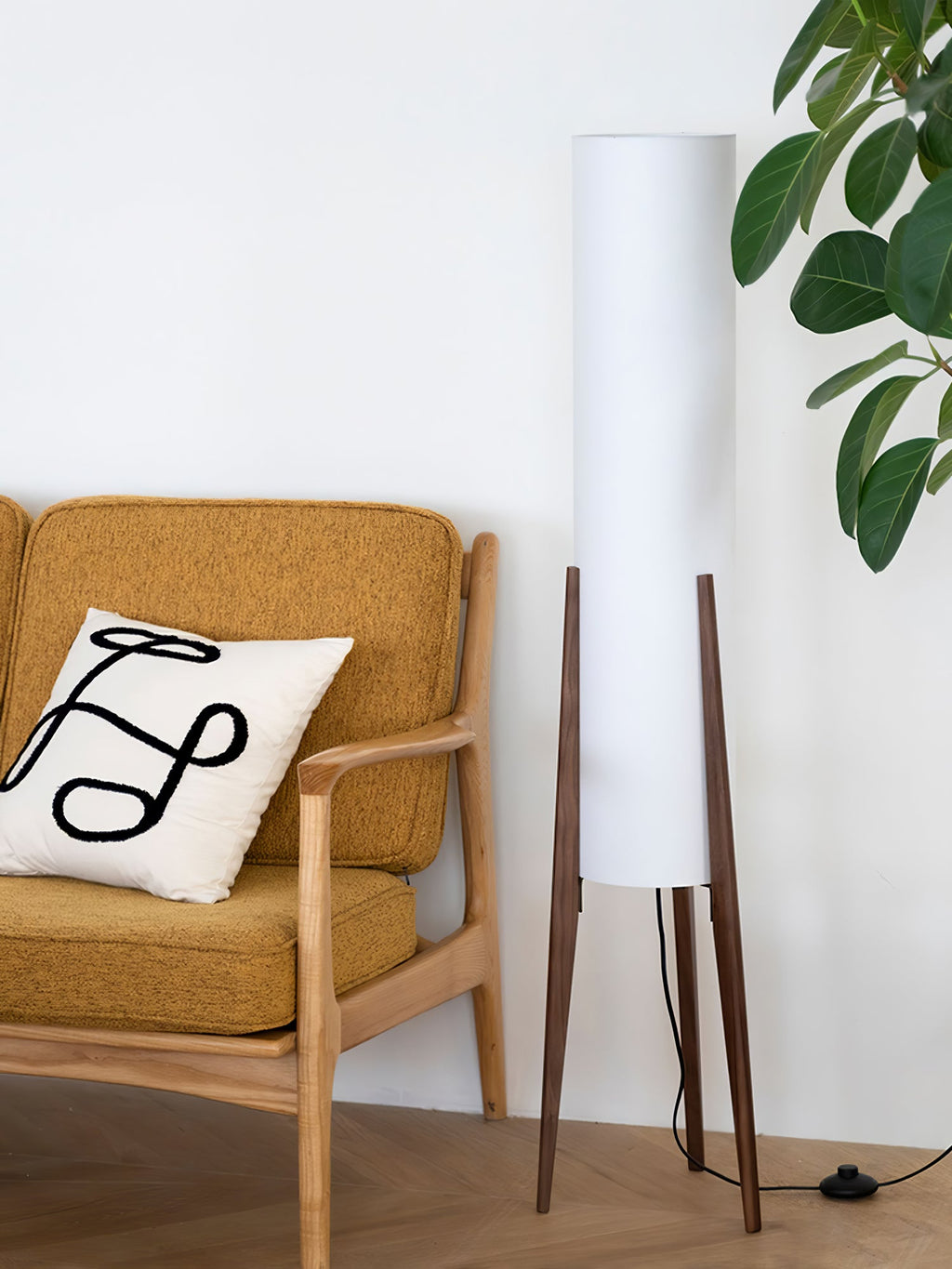 Walnut-legged Clérachic floor lamp with a white shade beside a mustard armchair with a cushion, and a leafy plant above.